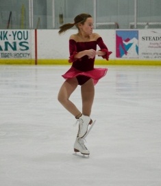 Girl in red skating dress performing jump in ice rink