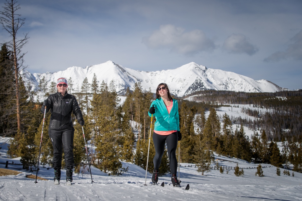 Two women Nordic skiing with mountains in background