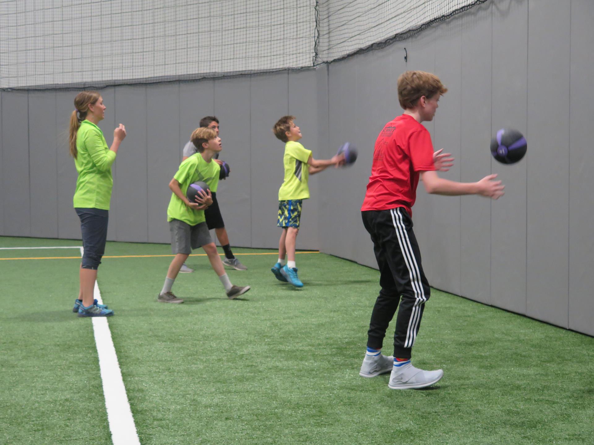 Teen boys and trainer excercising with medicine balls in turf gym