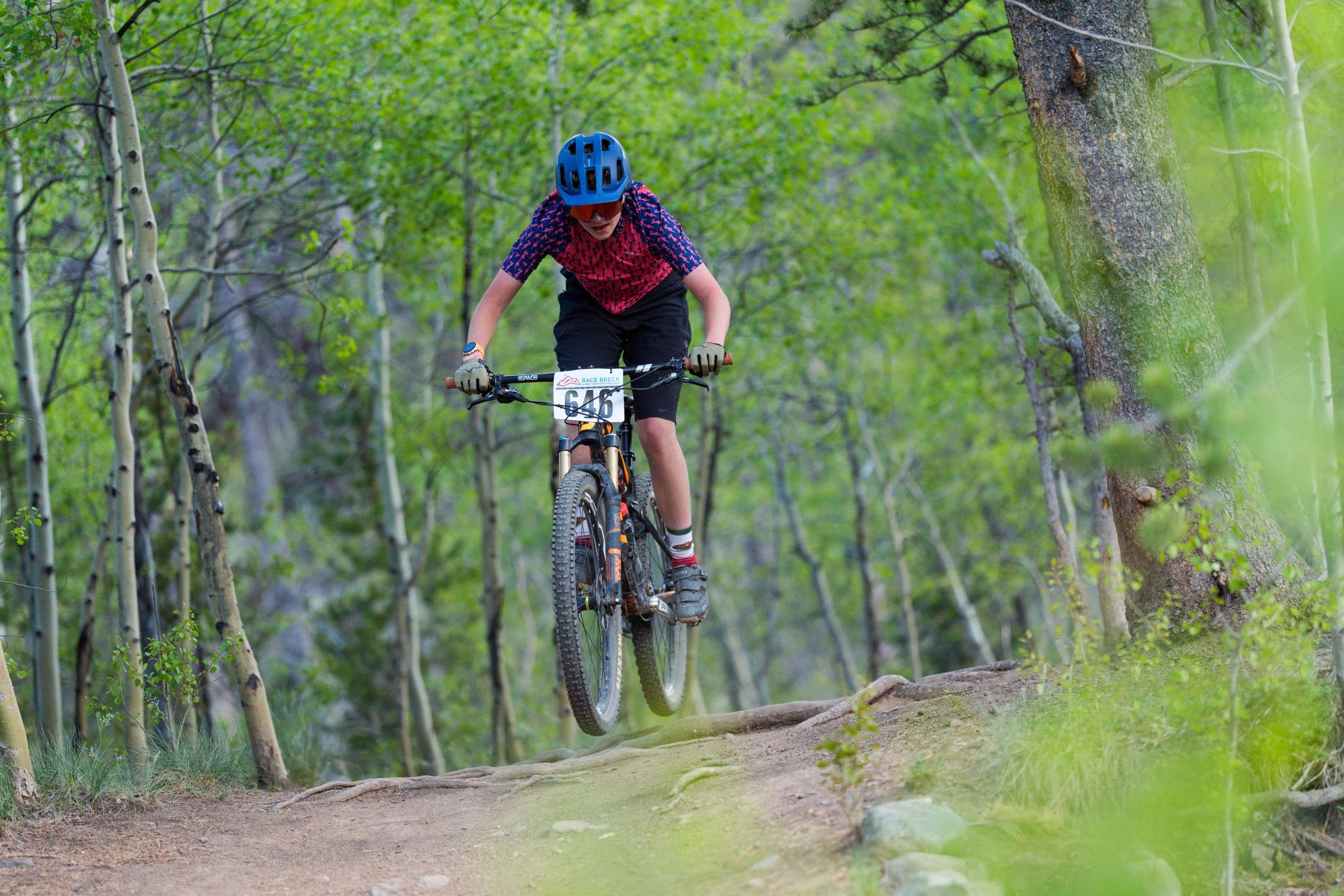 boy in pink and blue shirt wearing a blue helmet riding their bike