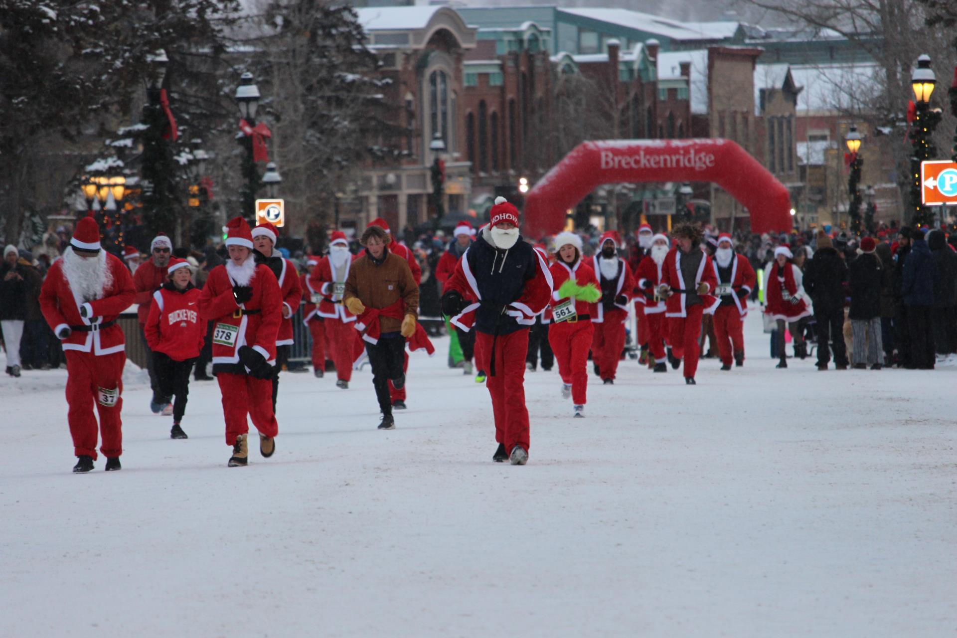 multiple runners in santa suits running down mainstreet in the snow